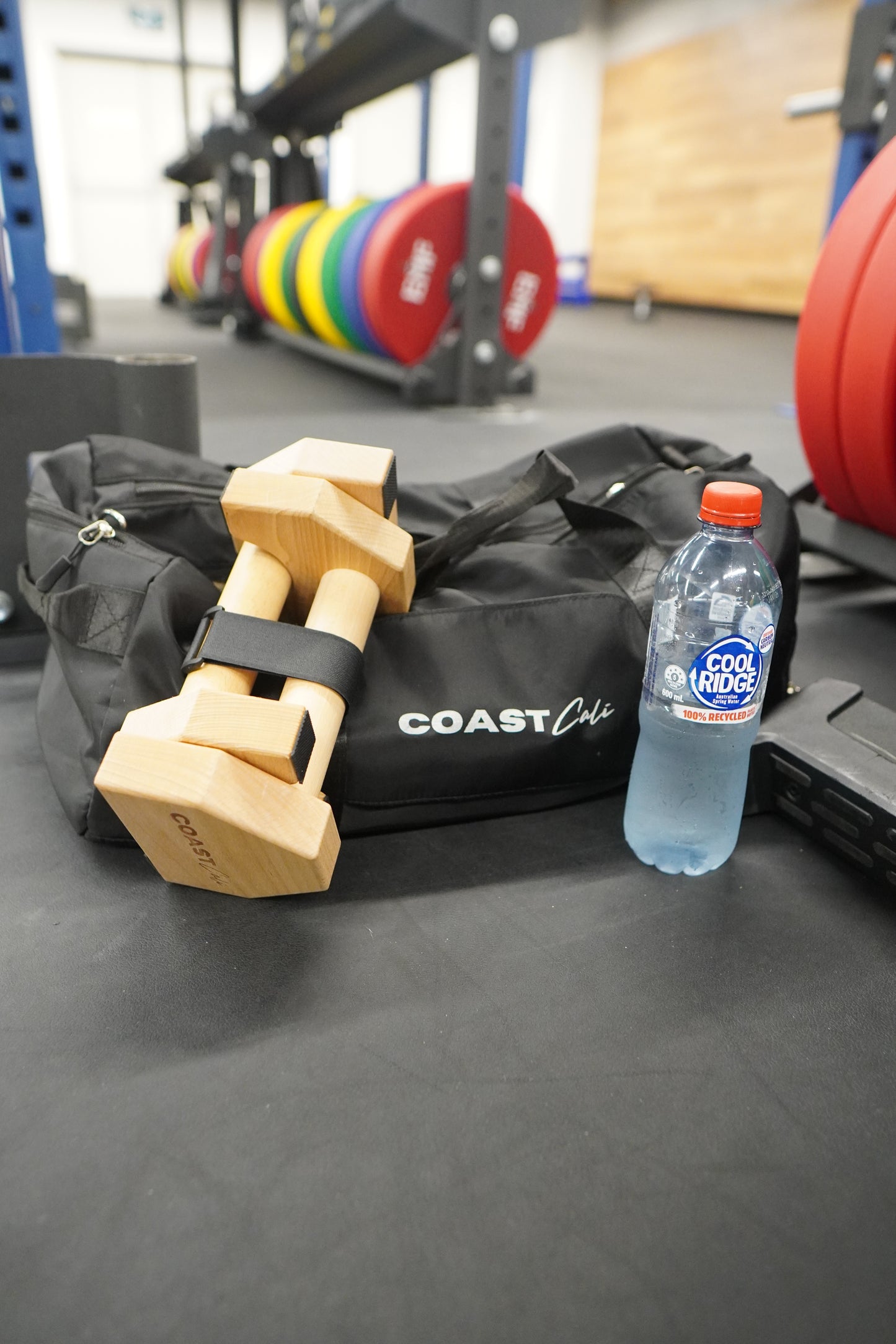 A pair of wooden travel parallettes alongside a duffle bag and drink bottle