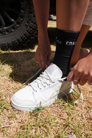 A woman tying up her shoes with black socks on