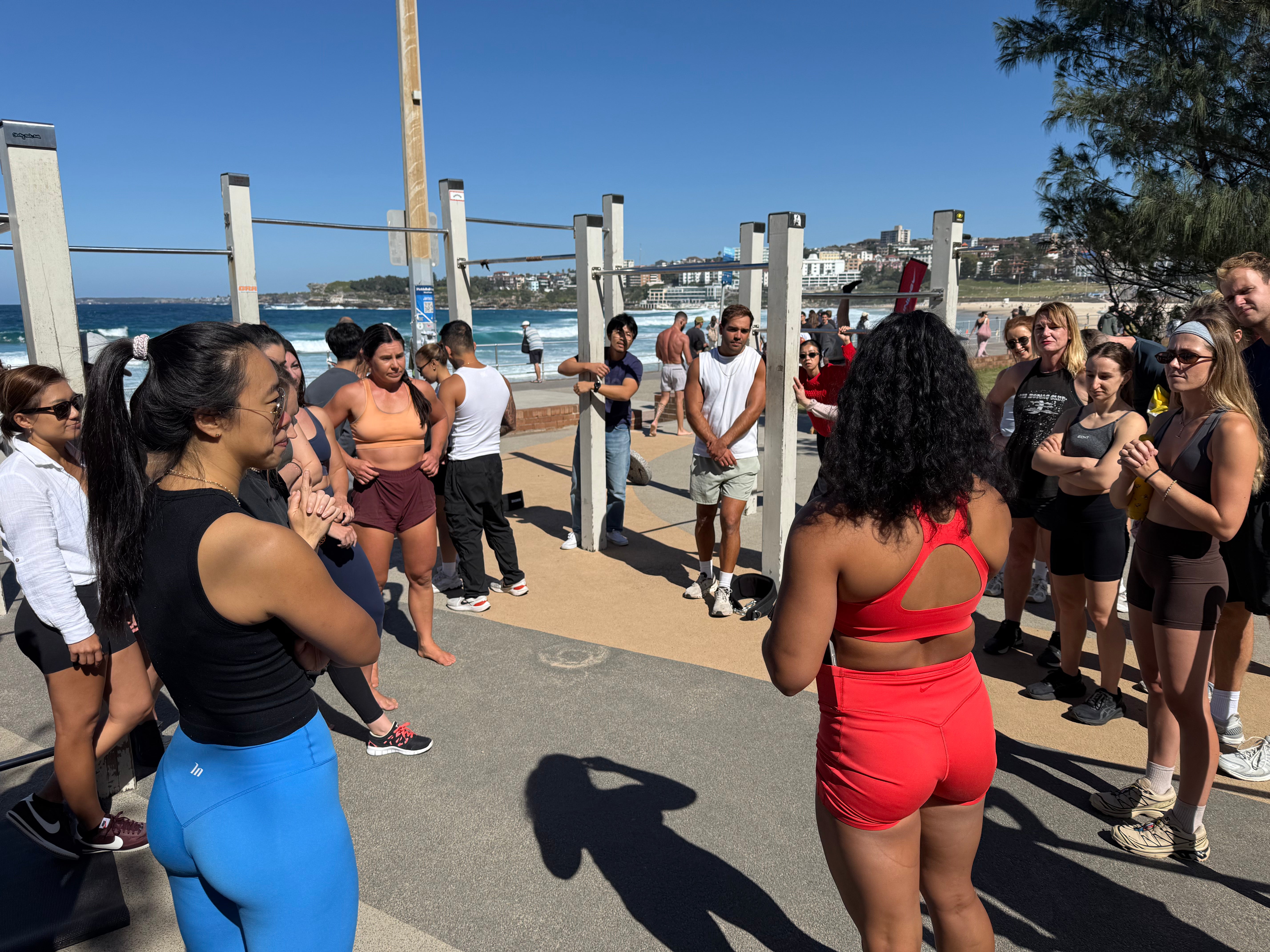Group of people exercising outdoors near a beach with ocean and skyline in the background.