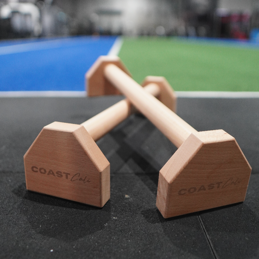 A close up of gymnastics parallettes with a gym in the background