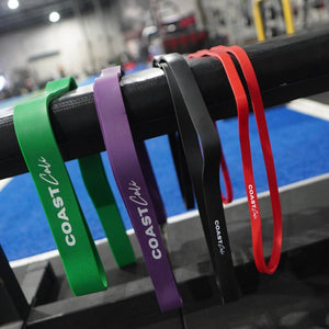 A set of 4 calisthenics resistance bands with 'Coast Cali' logo and gym in background