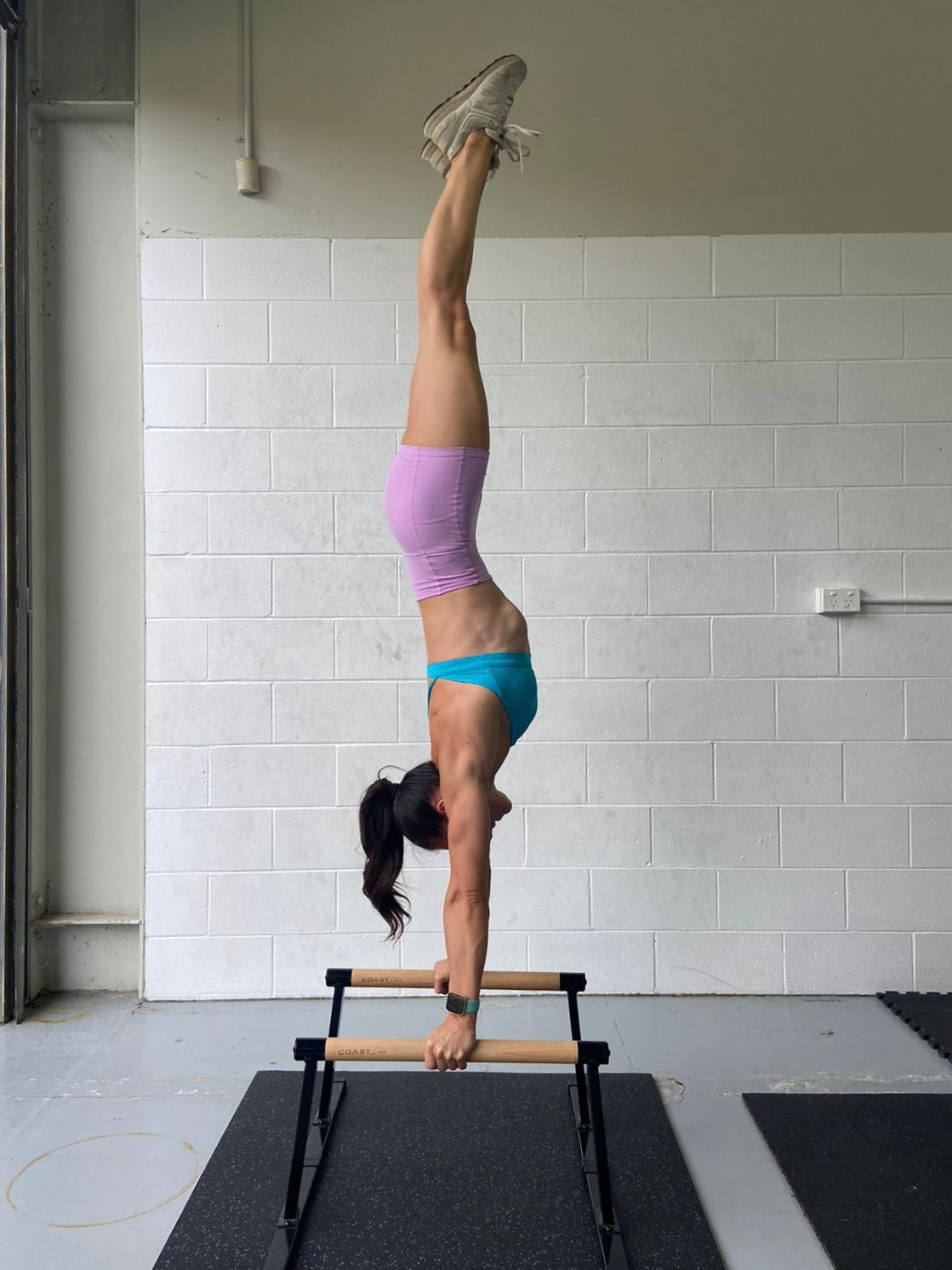 A woman doing a handstand on parallettes