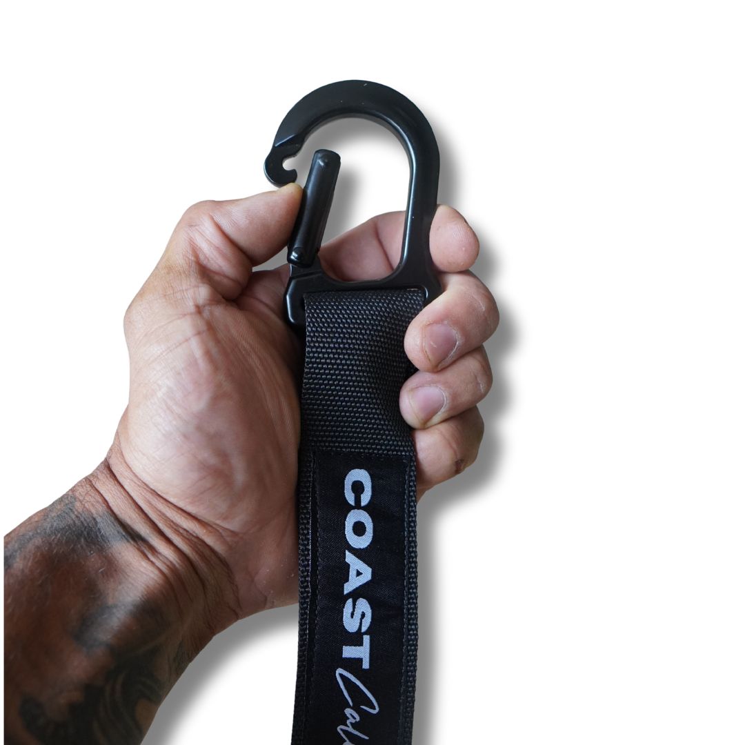 Hand holding a black strap with a carabiner, branded 'Coast Callis', on a white background
