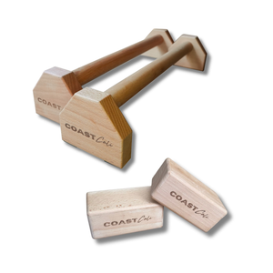 Two wooden dumbbell-shaped blocks with triangular end plates, shown on a white background with two additional blocks. The blocks are light natural wood with the brand name 'COAST Cali'.