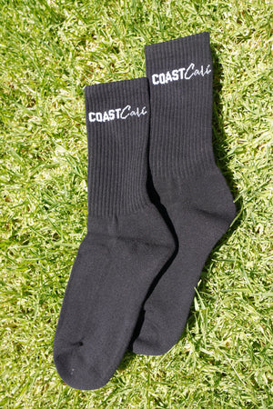 A pair of black socks on grass with the logo 'Coast Cali' on them