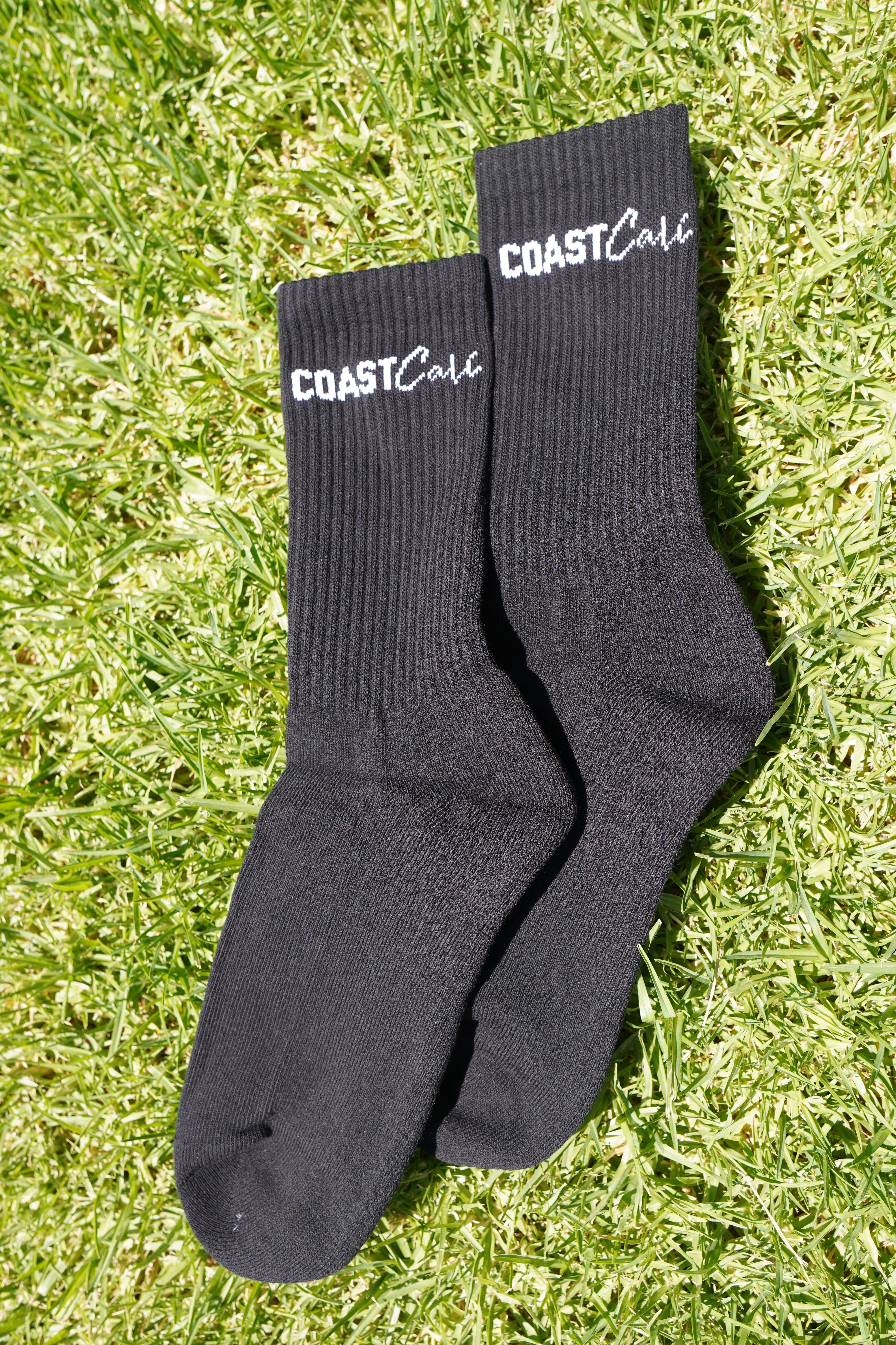 A pair of black socks on grass with the logo 'Coast Cali' on them