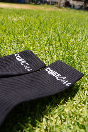 A close up of black socks on grass with the logo 'Coast Cali'