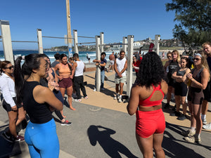 Group of people exercising outdoors near a beach with ocean and skyline in the background.