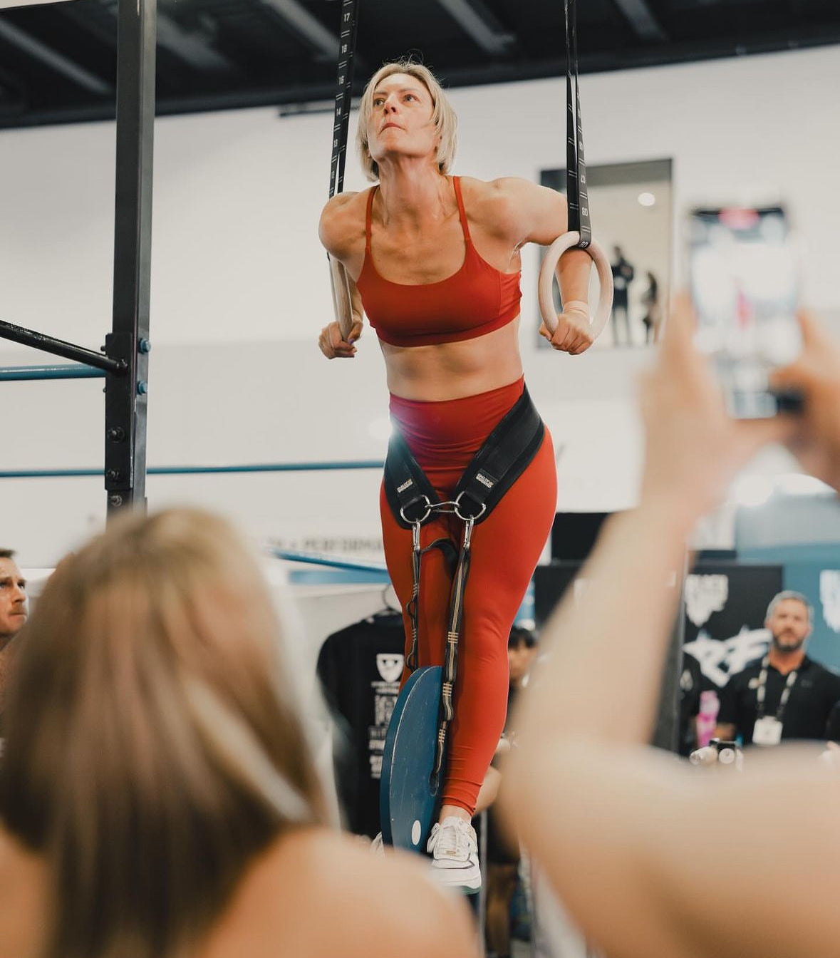 Woman performing on gymnastic rings in a gym setting with spectators.