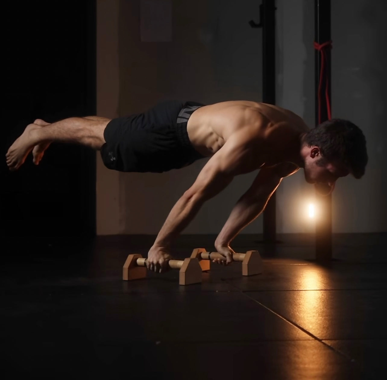 A man doing a planche on a set of parallettes