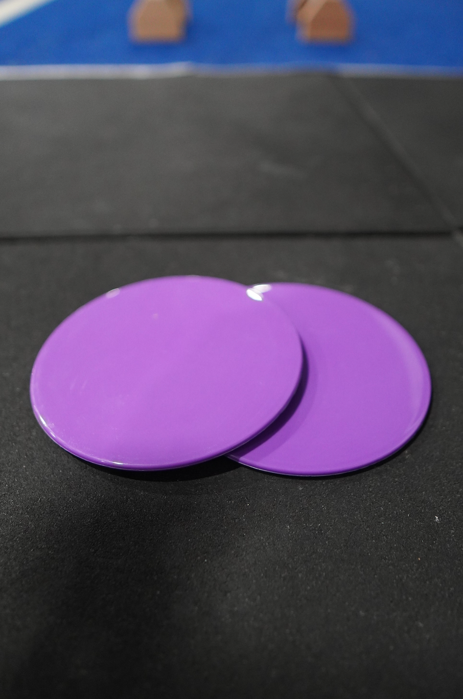 Two purple gymnastics sliders with the logo 'COAST Cali' on the top surface in gym
